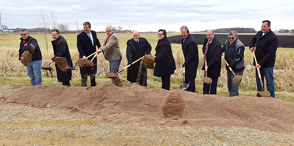 Ten men and women, each with a shovel in their hands, scoop sand from a large pile lined up in front of them